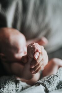 Parent holding baby's hand while considering options for bassinets that move | babybay bedside sleepers