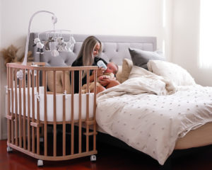 Mother feeding her baby next to a natural wood crib | babybay bedside sleepers