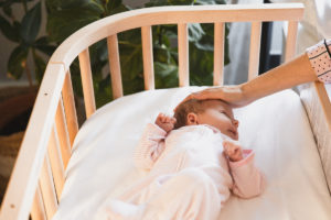 Baby in bedside co-sleeper being comforted by mother | babybay co-sleeper crib