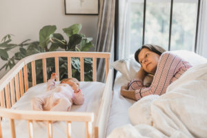 Mother next to baby who is lying in baby bed that converts to side bed bassinet | babybay bedside sleeper