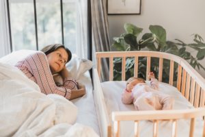 Mother watching baby sleeping in wooden bedside bassinet | babybay bedside co-sleeper