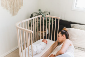 A mother watching her sleeping baby after figuring out how to get sleep with a newborn | babybay bedside co-sleepers