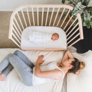 Parent happily watching baby sleeping on back in co sleeper | babybay bedside bassinets