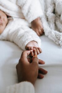 A mother touching hands with her baby in a co-sleeper bed | babybay bedside bassinets