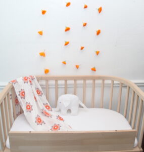 A baby beside sleeper with flower decorations above| babybay cosleepers